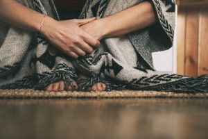 feet and hands of woman sitting on the floor wearing handmade poncho. copy space.