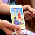 Mystic: Tarot card reader shows card pulled from deck to person having reading.